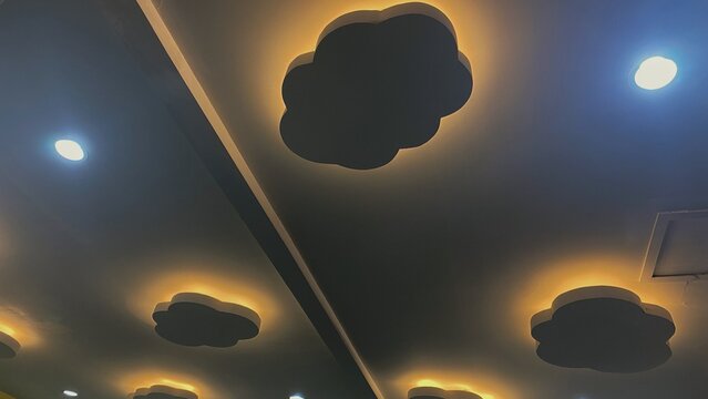 Modern ceiling interior with cloud-shaped decorative lights that emit warm light, combined with minimalist downlights.