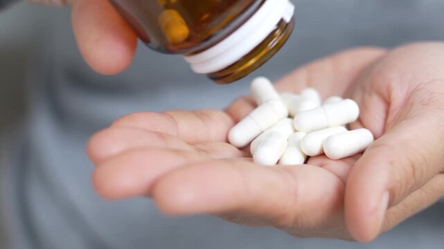 close up woman hand holding a medicine, with pours the pills out of the yellow orange medicine bottle. Stop drug use Taking Medication Caring for the health care medical concept.