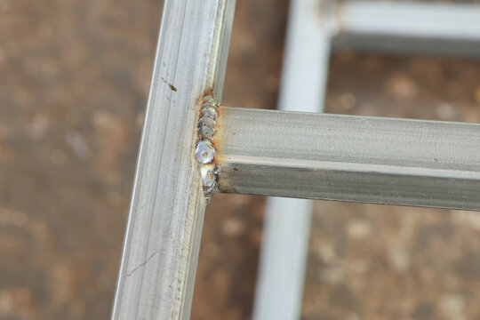 Close up view showing strong metal weld joint connecting square tube sections for an industrial steel or aluminum structure construction, displaying reliable and secure framework engineering