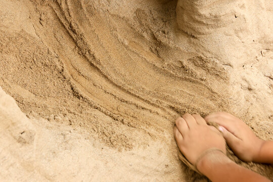 Close up of small child hand engaged in creative play digging wet sand and mud during summer beach vacation displaying playful focus on raw earth texture and natural craft