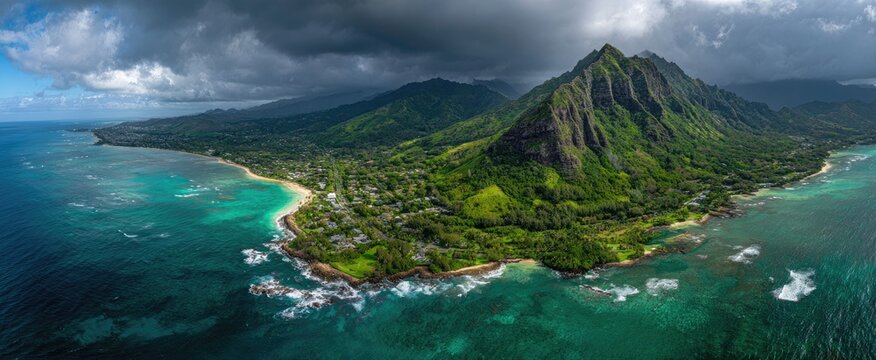 An aerial view showcases the stunning coastline of Oahu, Hawaii, featuring lush green mountains meeting turquoise waters under a dramatic, cloudy sky.