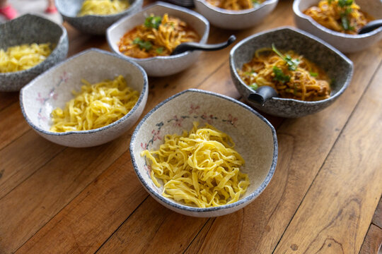 Delicious traditional northern Thai curry noodles khao soi in ceramic bowl on wooden table top view preparing for meal warm inviting feeling of local cuisine