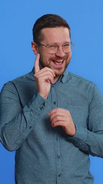 Sneaky cunning Caucasian middle-aged man in glasses with tricky face gesticulating and scheming evil plan, thinking over devious villain idea, cheats, jokes, pranks. Guy isolated on blue background