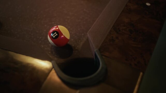 Top view shot of pool balls falling into pocket after successful shot during game on brown felt table in billiards club, slow motion