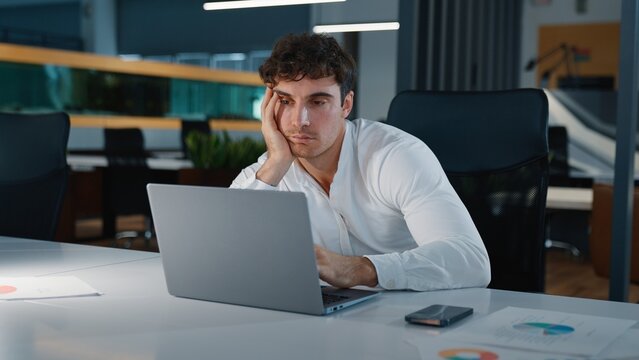 Boring sleepy tired Caucasian business man feeling bored looking in laptop unmotivated businessman male worker guy employer working with computer suffering boredom insomnia work at evening office