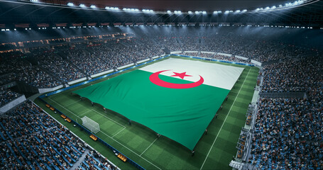 Fototapeta premium Professional Stadium Soccer Game Championship With Flag of Algeria Spread Across the Pitch Before Football Match Start. Cheering Crowds of Fans Surround the Field. Aerial Wide Shot
