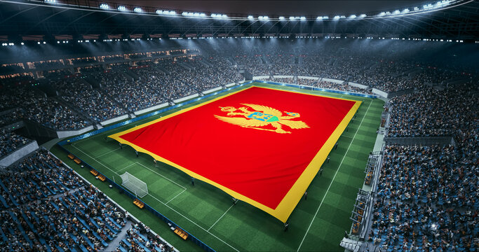 Professional Stadium Soccer Game Championship With Flag of Montenegro Spread Across the Pitch Before Football Match Start. Cheering Crowds of Fans Surround the Field. Aerial Wide Shot
