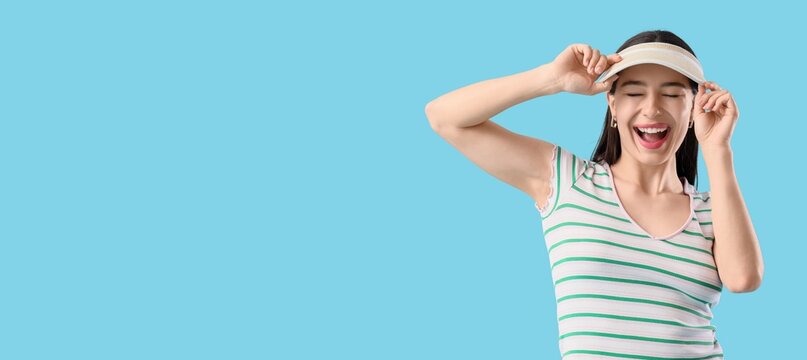 Stylish young woman in visor on light blue background with space for text