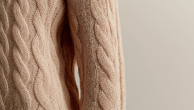 Close up of warm knitted sweater with cable pattern in soft beige tones. Cozy winter fashion fabric detail with copy space.