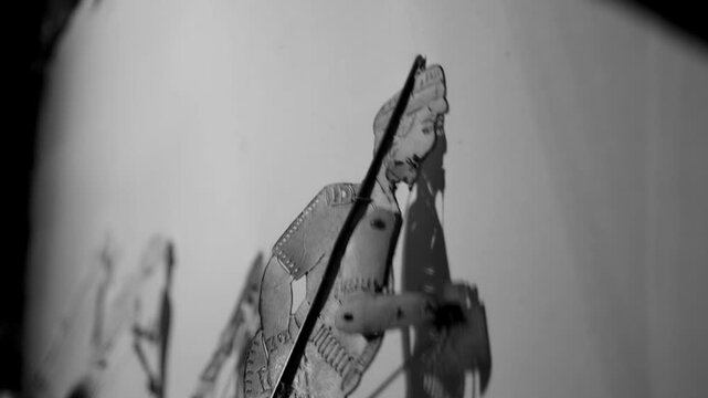 The black and white image shows hands manipulating a shadow puppet, a traditional art form of people in southern Thailand.