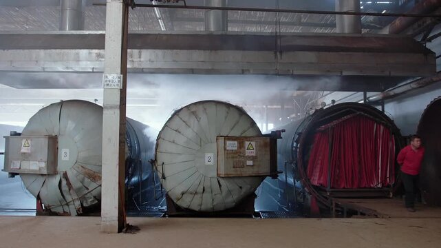 Chinese factory worker manually pulling a large red carpet out of an industrial steam machine