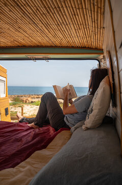 Woman reading book inside camper van at ocean