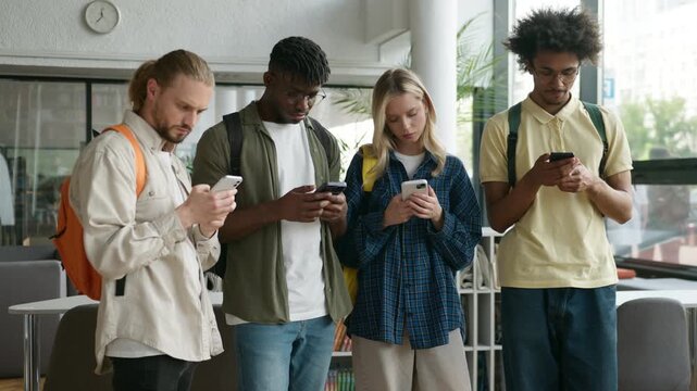 Four multiethnic students college university friends classmates gadgets addict overuse mobile phones apps modern technology playing virtual games in hall of academy ignoring busy with online addiction