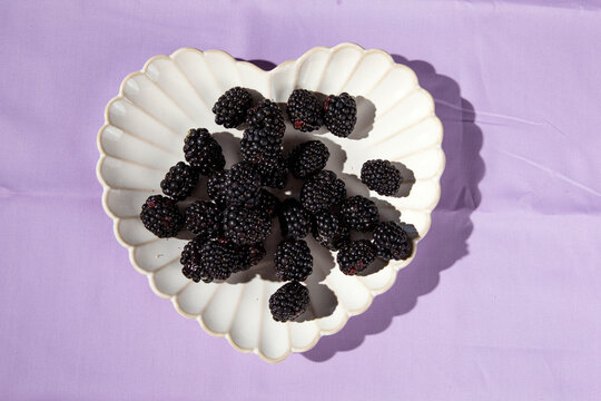 blackberries in heart plate on lilac cloth table top black blackberries