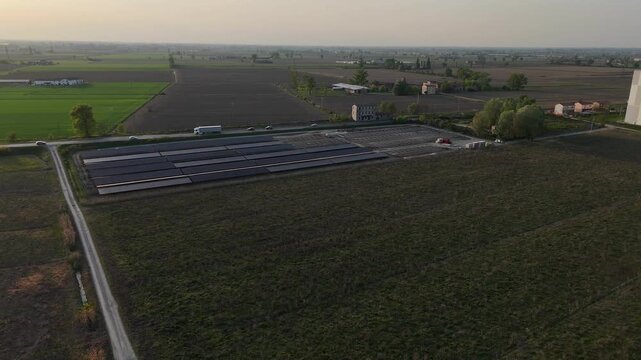 Solar farm along Via Emilia SS9 in Pianura Padana near Fiorenzuola d&rsquo;Arda Piacenza Emilia Romagna Italy with parallel panel arrays across farmland under sunset light, drone lateral pan left shot