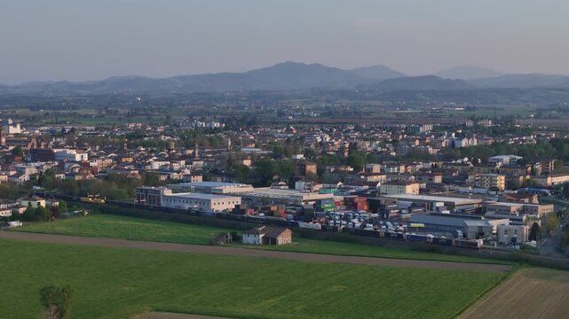 Freight train passing Fiorenzuola d&rsquo;Arda Piacenza Emilia Romagna Italy with town skyline and distant Ligurian Apennines ridge forming horizon within Po Valley landscape, drone lateral static shot