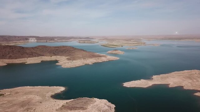 Cinematic drone shot showing the "bathtub ring" effect on the rocky shores of a desert reservoir, highlighting water scarcity and environmental impact