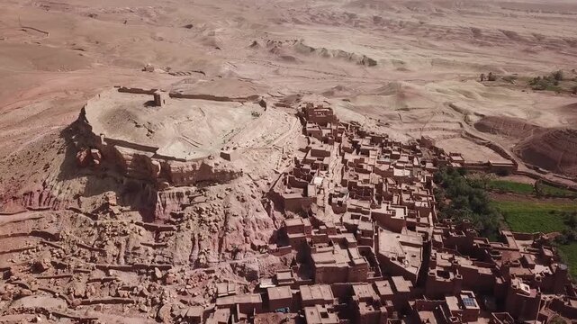 Drone view of Ait Benhaddou showing the historic kasbah and vast rocky desert plateau. Strong contrast between dense adobe village and barren landscape, ideal for cinematic and heritage visuals.