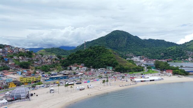 A sweeping drone shot showing the coastline, sandy beach, and lush green mountains of Angra dos Reis in Rio de Janeiro state.