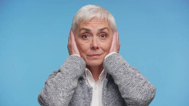 Senior woman covering ears in refusal on blue background