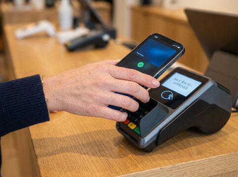 Customer completing a contactless mobile payment using a smartphone digital wallet at a point of sale terminal. Cashless transaction with tap-to-pay technology in a modern retail environment