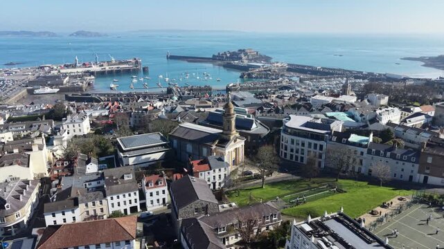 St Peter Port Guernsey,rising reveal of St James Assembly hall and Elizabeth College with views across the town,harbour ,Castle Cornet and to Herm Jethou and Sark with misty horizon in bright sun