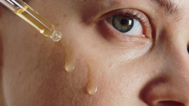 Woman applying liquid skincare serum with a pipette to her face, showing large droplets running down her cheek, emphasizing hydration, healthy skin, and anti aging cosmetic treatment