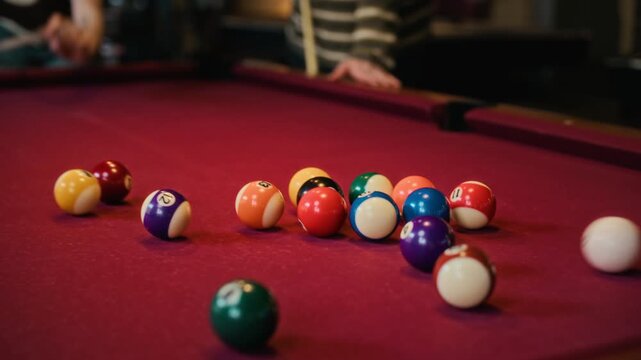 Rack focus shot of young adult woman breaking in billiards game striking cue ball into rack on red felt table while playing pool with friends at game room