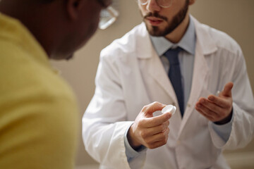 Fototapeta premium Close up of young adult Caucasian male doctor explaining usage of glucose monitoring sensor to Black man during consultation. Supporting healthcare communication, treatment guidance, patient education