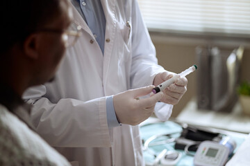 Close up of doctor preparing injection while Black male patient watching during medical...
