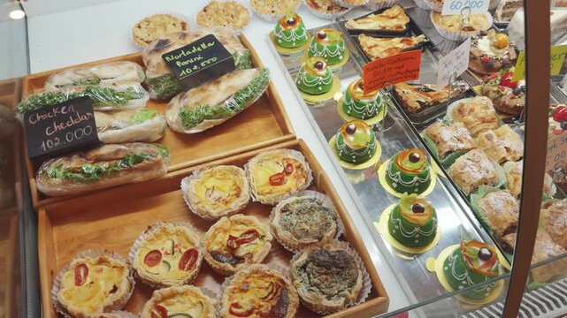 Display case showcasing a tempting variety of freshly prepared sandwiches, savory mini quiches, and elegant green frosted pastries, reflecting a vibrant food retail environment