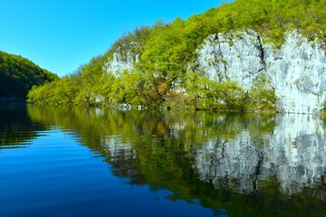 Obraz premium Rock cliff and green foliage above the lake with a reflection in the water in Plitvice national park in Lika, Croatia