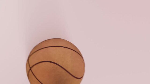 Dropping basketball passing through circular opening, rolling across pale pink platform, white rail