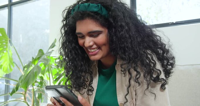 Woman getting alert, smiling while scrolling phone on couch then answering call by plant
