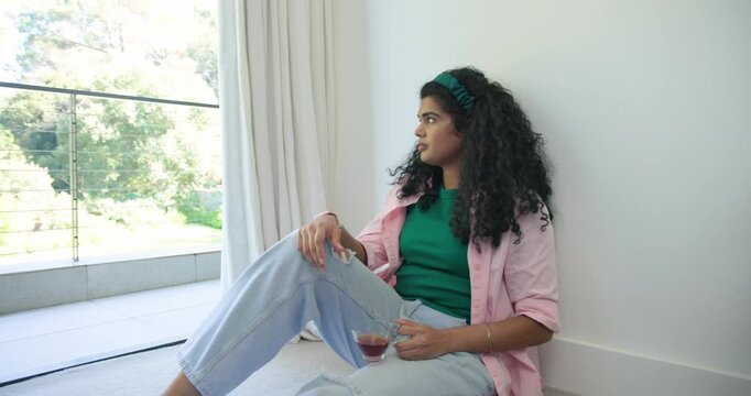 Adult woman sitting on floor by sliding glass door balcony view urging sipping stemmed glass gazing