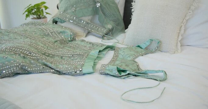 Camera is panning right toward bed, revealing embellished mint dress and dupatta to showcase bodice