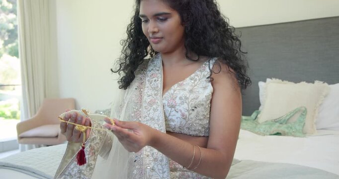 Indian woman sitting on bed dressing with dupatta and handling gold tassel while hearing sound