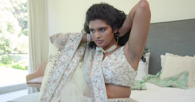 Indian woman preparing for event on bed adjusting hair fixing choker placing dupatta adding bangles