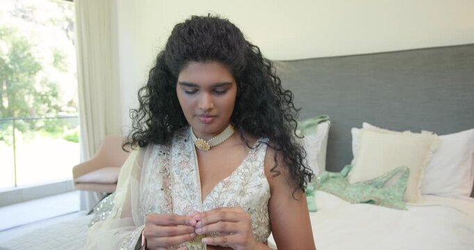 Adult Indian woman sitting on bed readying embroidered outfit, checking and adjusting yellow jhumka