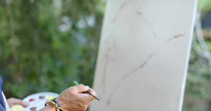 Senior Asian male aligning green-tip brush tracing brown-curves to form arches on canvas in garden