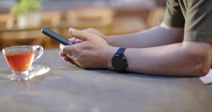 Senior Asian man starting hands resting, holding and swiping phone at table, teacup, watch, texting