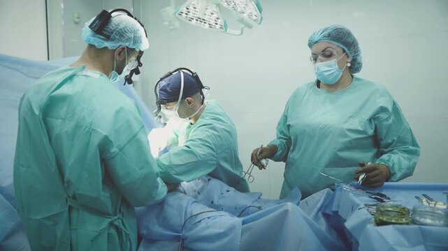 Three clinic workers in protective uniform surgeons doctors operating patient medicine health care procedure. Nurse woman help men practitioners operate at table malignant tumor remove surgery health
