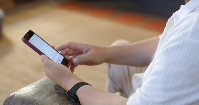 Senior Asian man holding purple smartphone tapping and reading on sofa leather armrest, copy space