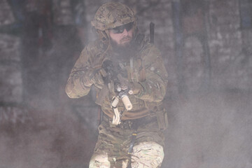 Obraz premium Armed Soldier In Camouflage Tactical Gear Moving Through Smoke During Urban Military Operation