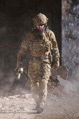 Obraz premium Armed Soldier in Tactical Gear Walking Through Dusty Urban Ruins During Military Operation