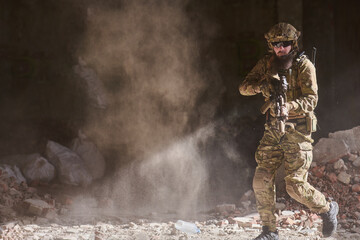Obraz premium Armed Soldier In Tactical Gear Moving Through Dusty Urban Ruins With Rifle Ready