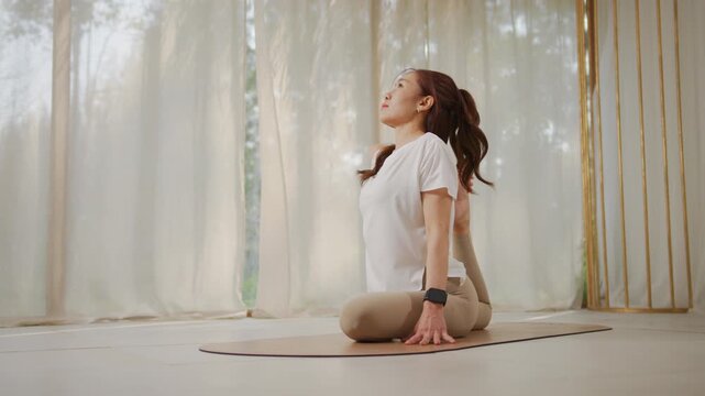 Yoga pose woman stretching on mat in bright indoor studio near curtain with calm natural window light, serene indoor yoga stretch pose for relaxation and balance