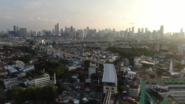 Jakarta, Indonesia - April 26th 2026: Aerial View of Densely Populated Residential Area and Skyscrapers under Hazy Golden Sunset. Urban Landscape Featuring Elevated Rail Infrastructure and Modern City