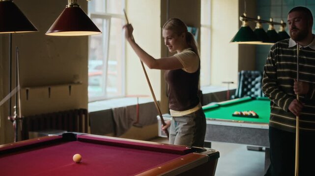 Dolly away shot of young adult woman taking break shot in billiards game while playing pool with friends at entertainment venue