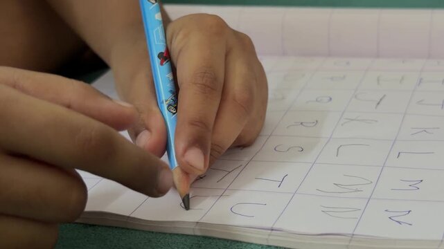 Close-up of child practicing alphabet writing with pencil on notebook, early education learning, handwriting skills development